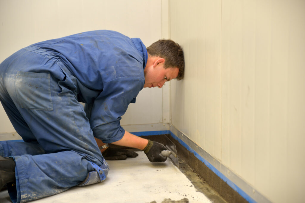basement repair contractor applying waterproofing product to floor of home during basement foundation repair